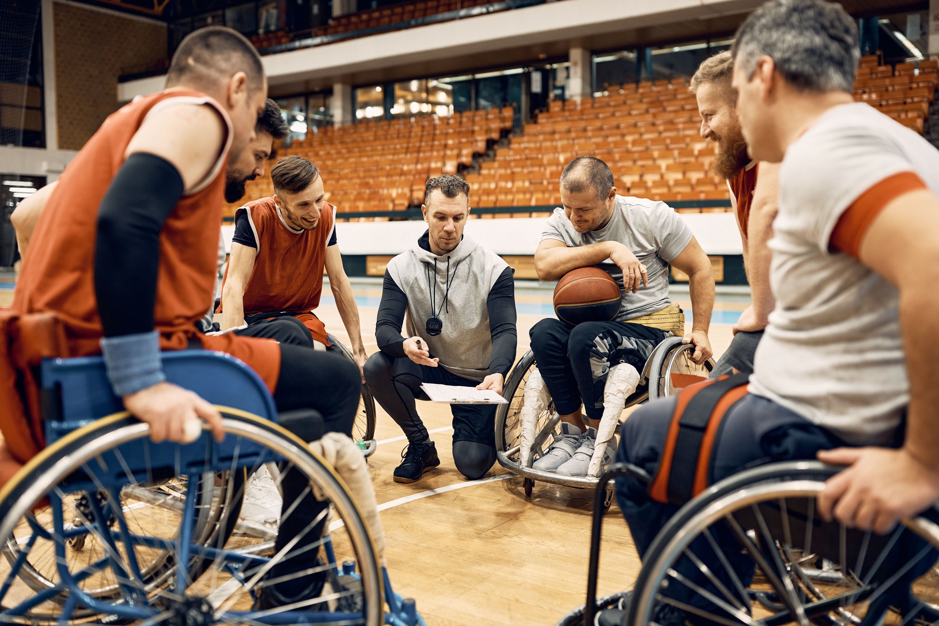 Coach of wheelchair basketball and his disabled players going through game strategy on the court.