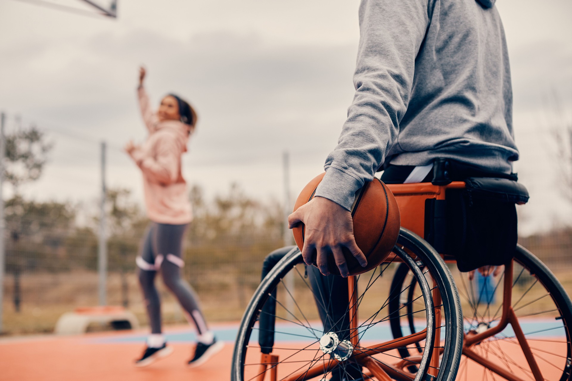 Unrecognizable athlete in wheelchair holding basketball on outdoor sports court.